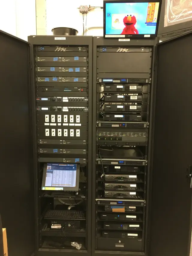 Audio and video equipment racks with a monitor displaying a children's show character, showing various electronic components and a computer keyboard.