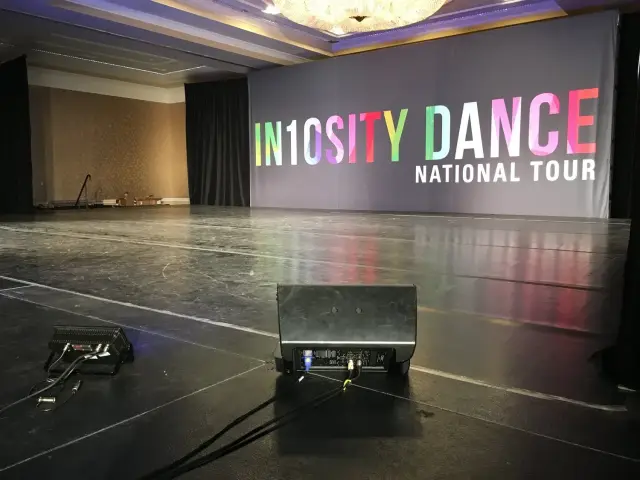 Empty dance stage with "IN10SITY DANCE NATIONAL TOUR" backdrop in a performance venue.