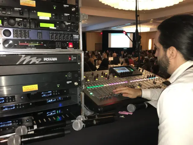Audio technician operating mixer at event with audience.