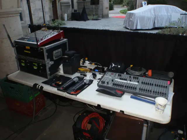 Audio equipment setup with sound mixer, microphones, cables, and other accessories on a table in an outdoor setting.