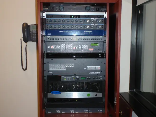 Server rack with audio and video equipment and a wall-mounted telephone.