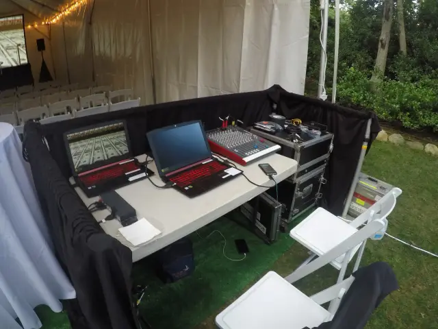 Audio-visual equipment setup under a tent with a laptop, sound mixer, speakers, and chairs.