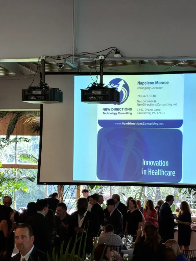 A presentation event with a large screen displaying a speaker slide for Napoleon Monroe, Managing Director at New Directions Technology Consulting.