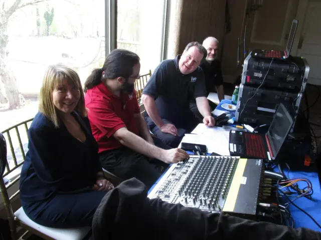 Four people sitting at a table with audio equipment and laptops.