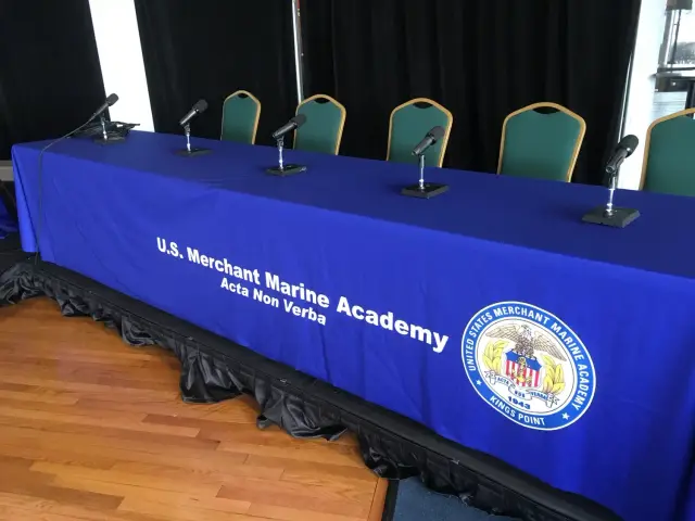 Panel table with blue tablecloth labeled "U.S. Merchant Marine Academy" and microphones.