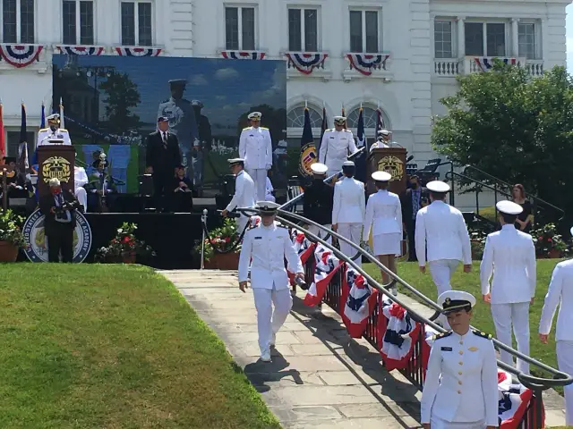 Military academy graduation ceremony with officers in white uniforms and patriotic decorations.