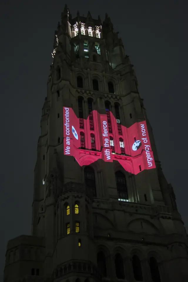 Gothic-style church tower with illuminated text and graphics projected on it at night.