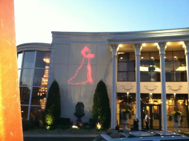 Exterior of a formal event venue with columns, decorative lighting, and a red dress stencil projected on the wall.
