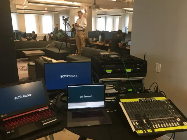 Office setup with laptops and audio equipment in a modern office, featuring people working and a person with a camera.