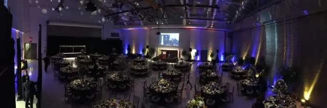 Large banquet hall with decorated tables, stage with podium, and ambient lighting.