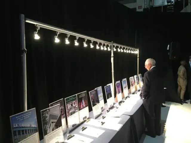 Man viewing an exhibit table with information displays and clipboards under overhead lighting.