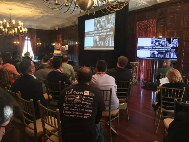 Audience at a security conference in a wood-paneled room, listening to a speaker.