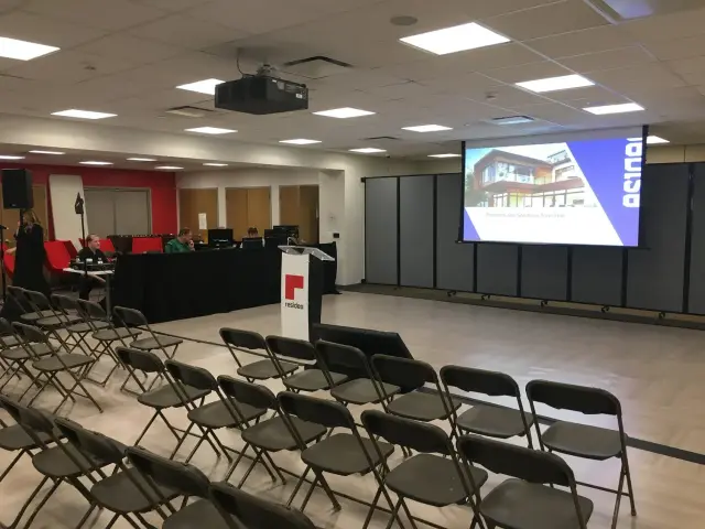 Empty conference room with rows of chairs facing a projector screen and podium, prepared for a town hall meeting.