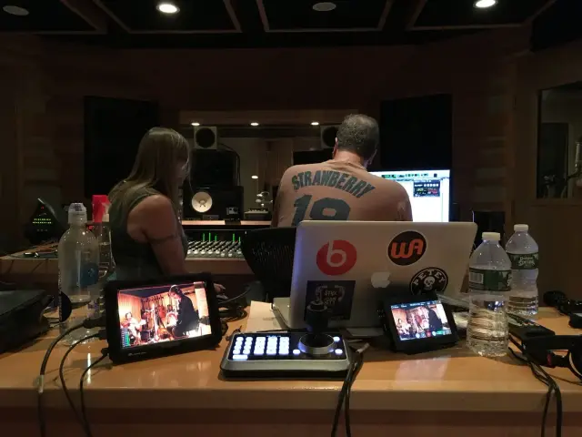 Recording studio with people working at a mixing console, computer screens, audio equipment, and water bottles.
