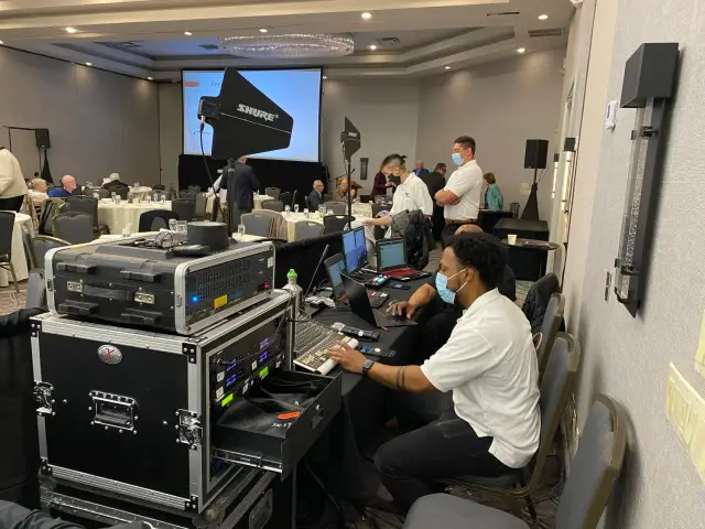 A conference room with audiovisual equipment and staff setting up for an event.