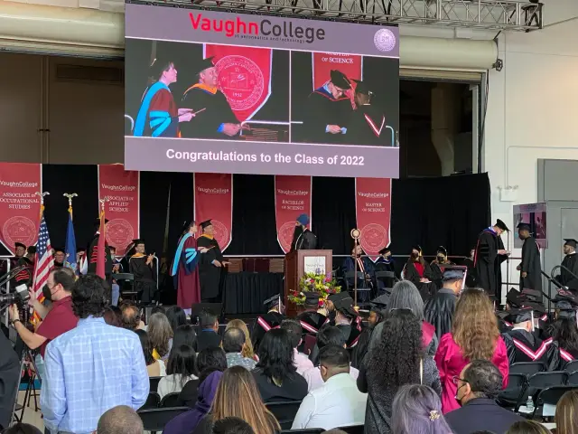 A graduation ceremony at Vaughn College, featuring students in caps and gowns receiving diplomas.