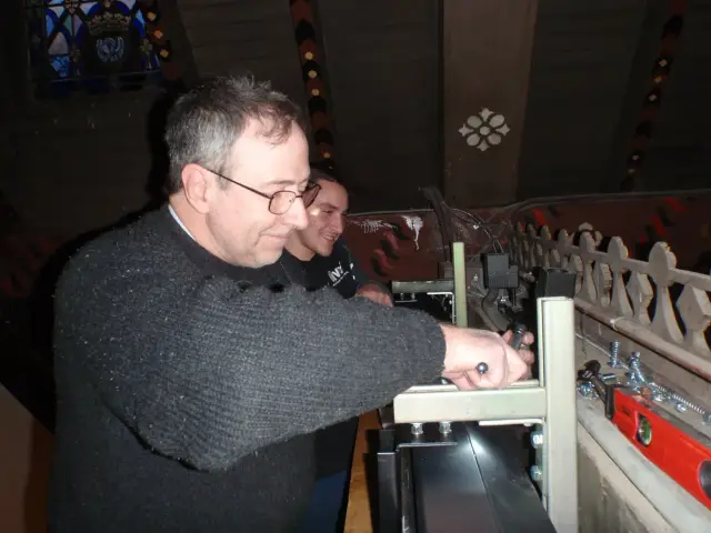Two individuals working with tools on an equipment setup in an attic-like space.
