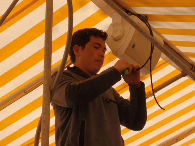 Person installing a speaker under a yellow and white striped awning.